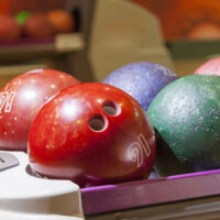 A close-up of six plastic bowling balls in different colors on a ball return found at local bowling alleys.