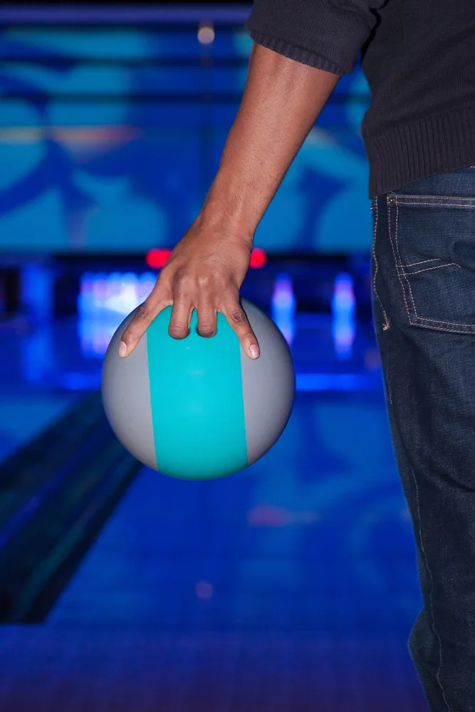 Man standing at the foul line with a gray bowling ball with a turquoise stripe in the center released his roll and cleared the split for his bowling league.