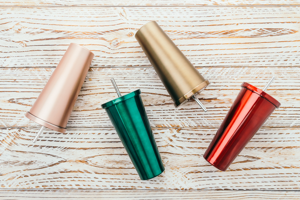 Four tumblers rose gold, green, gold and red on a wooden background are things the bowler can carry with them.