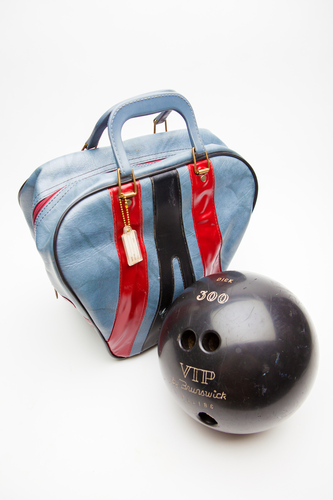 A sky blue bowling bag with two red stripes and a single black stripe on the front. Bowling bags come in different sizes and shapes.