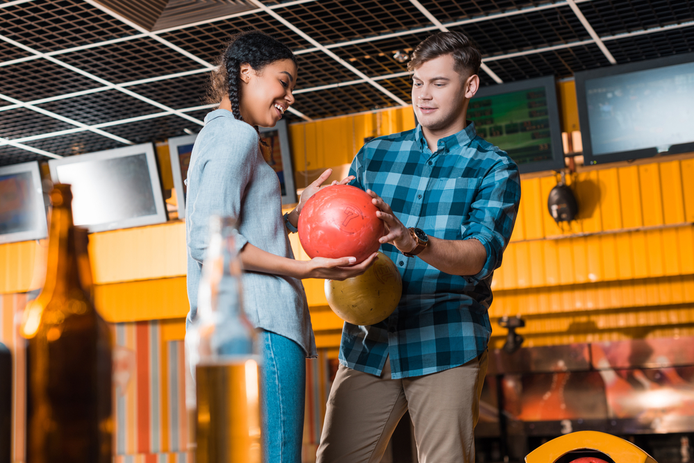 The girl in the blue shirt holds her bowling ball as she receives instructions.
