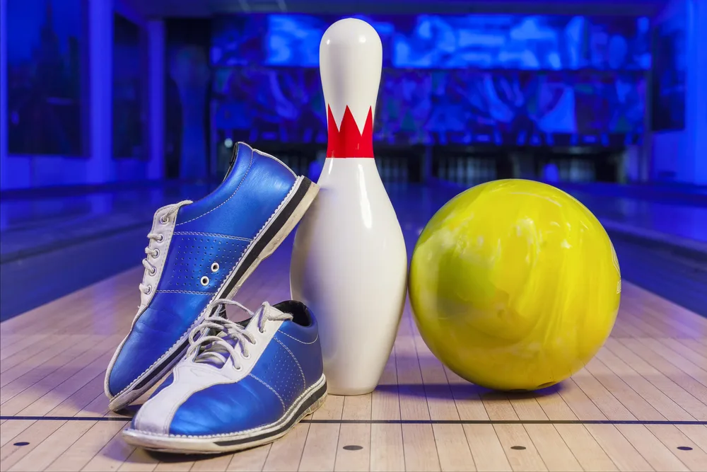 Two colored, white and blue, bowling shoes with a bowling pin, and a yellow bowling, are slick shoes, that are made for bowling.