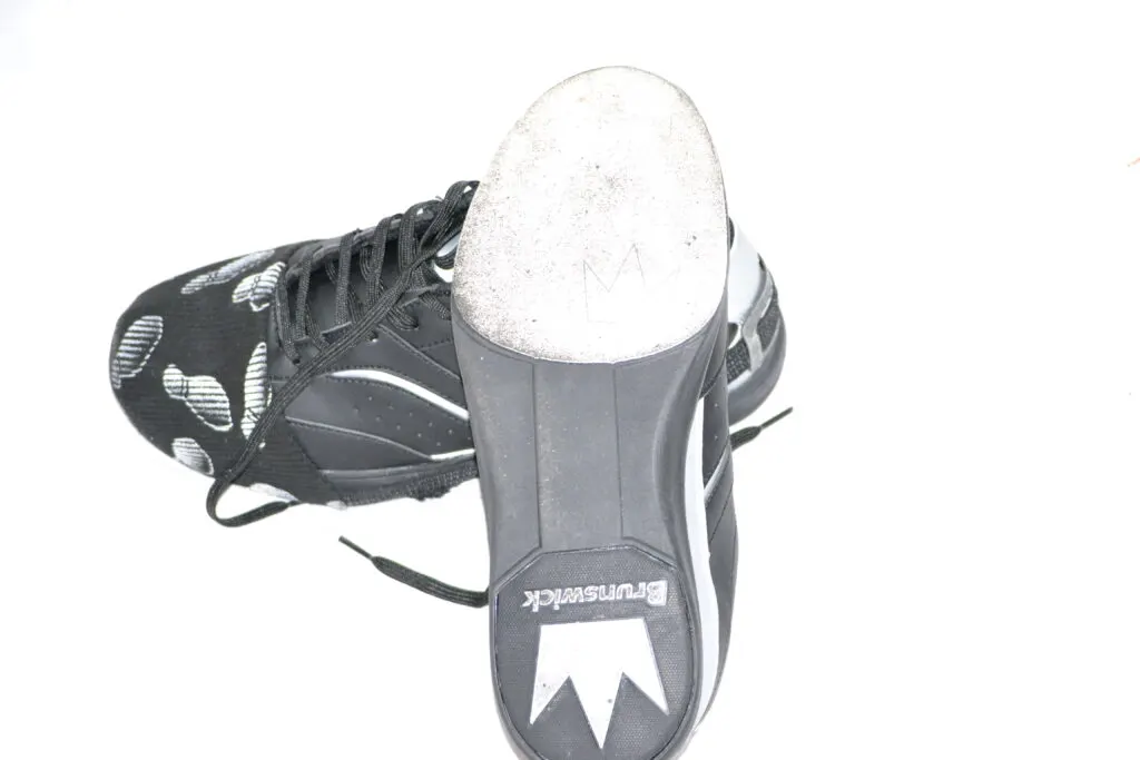 The black and gray brunswick bowling shoes, on a white background, have a soft cloth sole because it is mandatory to wear bowling shoes.