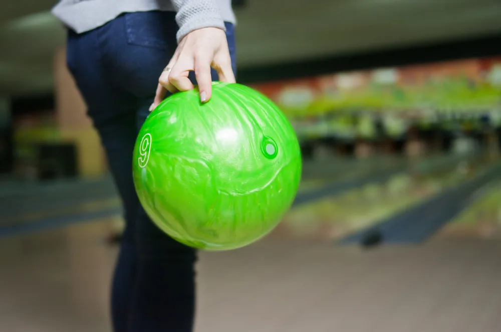 Woman's hand holds a green bowling ball, ready to throw with her thumb in the ball's thumb hole and using fingertip grips for the middle and ring fingers.