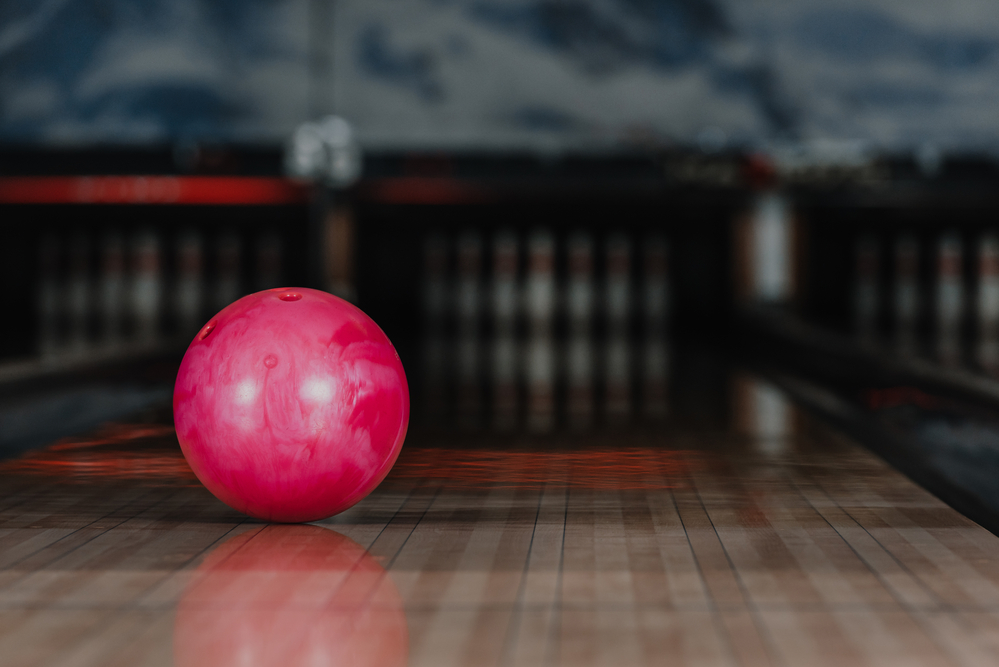 Pink bowling ball on the bowling lane that was released using the hook bowling technique.