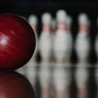 A red bowling ball thrown towards ten pins standing as a bowler goes after a perfect game without any open frames.