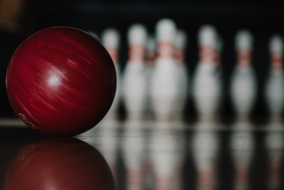 A red bowling ball thrown towards ten pins standing as a bowler goes after a perfect game without any open frames.