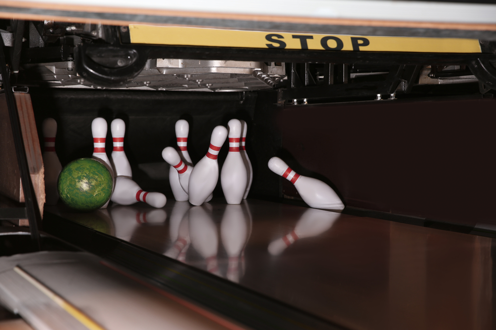 The bowler rolls the green bowling ball down the lane, missing the pocket with a weak hit and hitting the rear pin, leaving a cluster of three pins 2-4-5.