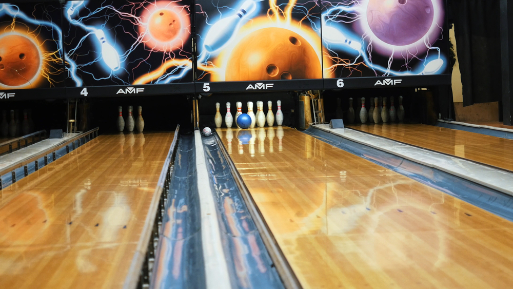 A blue bowling ball hitting the bowling pins on a lane. A ten-pin bowling pin lies in the gutter and the adjacent lane has their black bumper rails erect, giving a rich upscale look, made from a strong, durable pvc material.