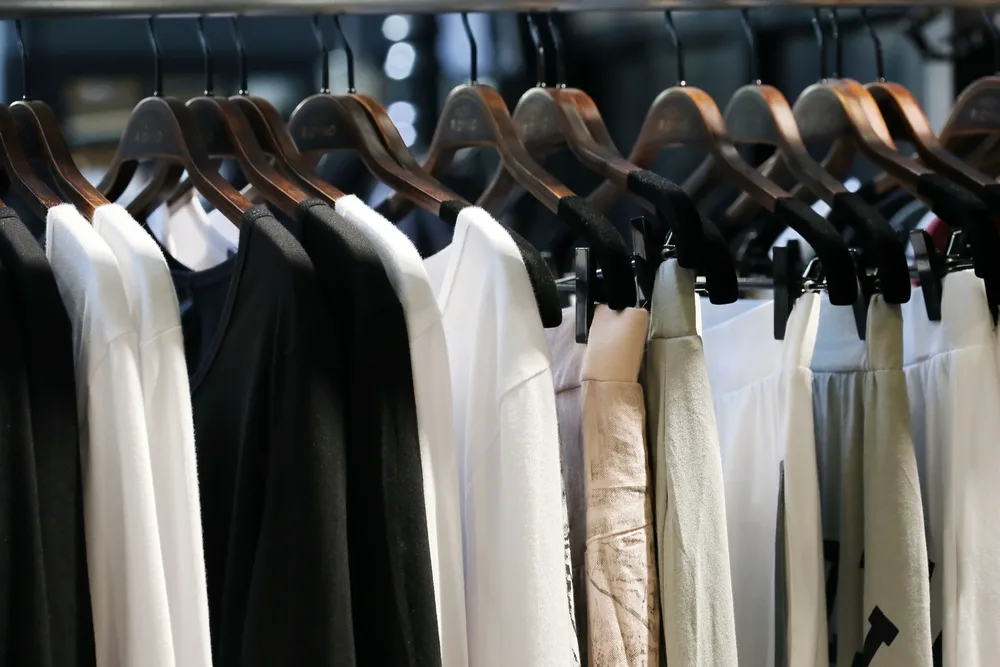 Clothes hanging in a closet on hanger includes a leather jacket, white tee, skinny jeans and a t shirt.