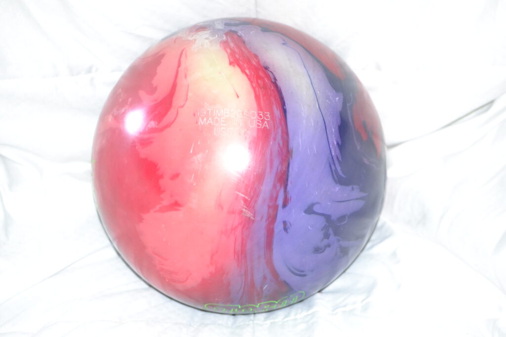 Red, blue and purple storm bowling ball sitting on white background.