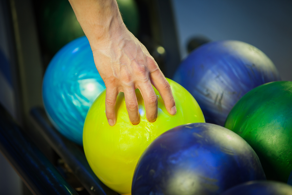 Man reaching for yellow pyramid bowling ball on the ball return. Pyramid is a relatively new brand in the bowling community.