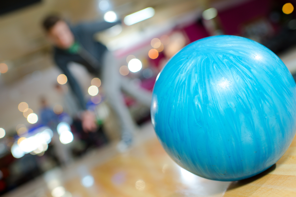 The bowler lined his dominant foot and rolled the blue ball in the bowling competition, hitting all ten pins.