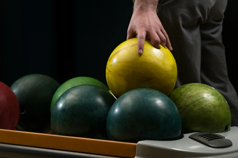 Man picks up his yellow spare ball from the ball return.