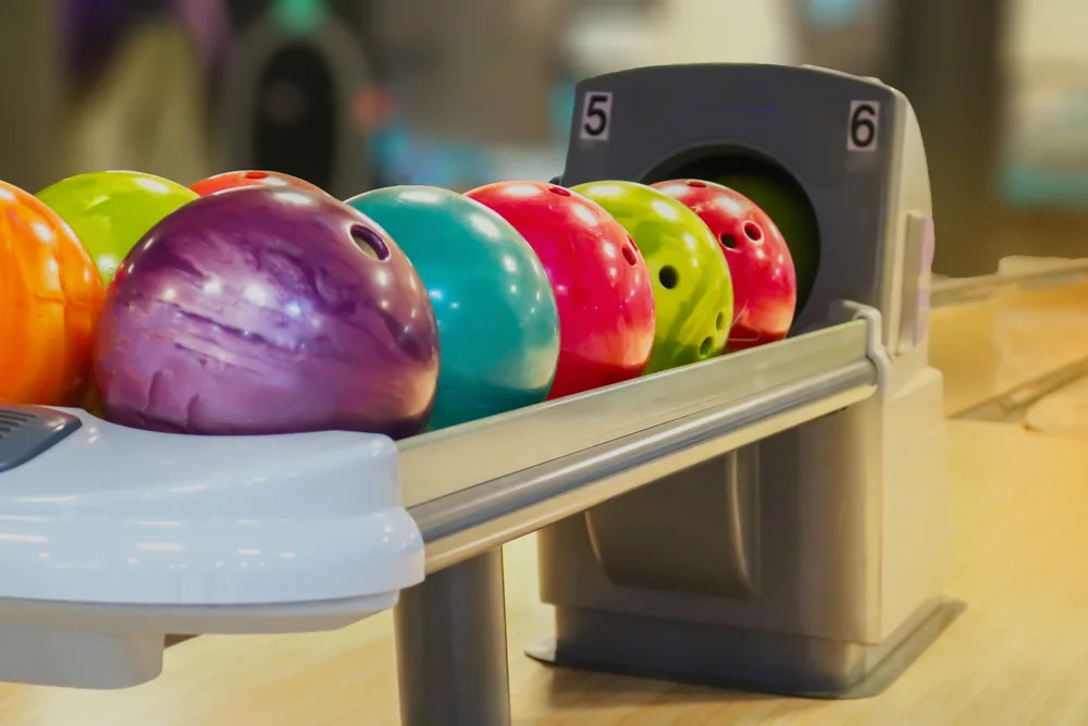 Multiple bowling balls sitting on a ball return at the bowling alley.