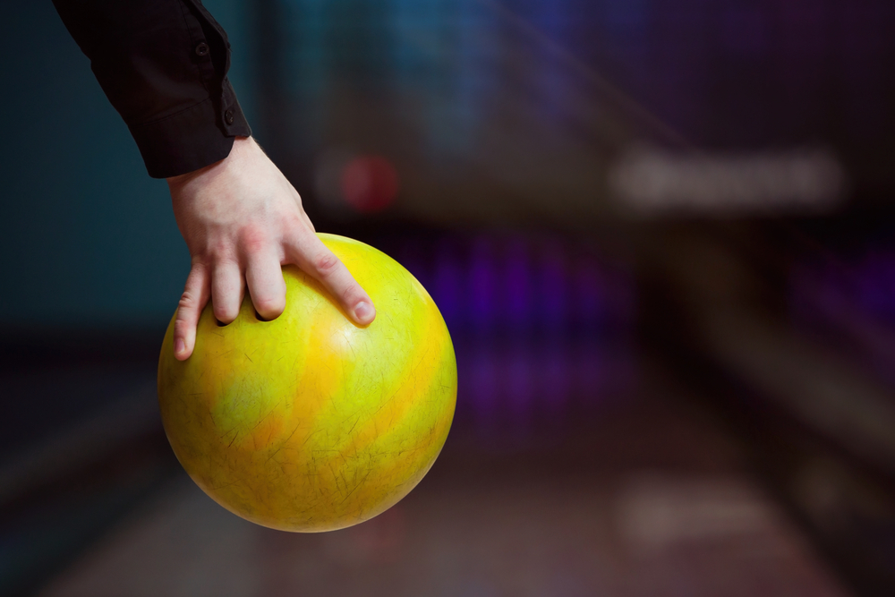 The bowler, wearing a black shirt, approached the line with their yellow ball, instead of using one of other bowling balls.