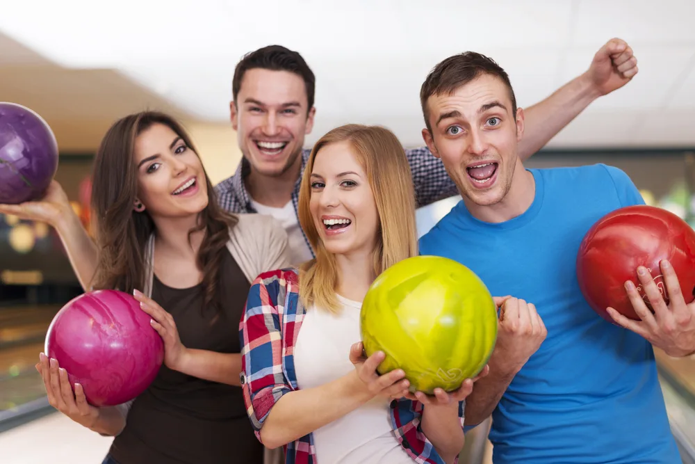 Friends in a group picture holding colorful bowling balls at the alley.