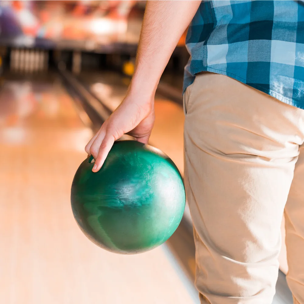 A person standing in the approach holding a green bowling ball with their fingers inserted.