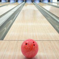 A bowling ball in a bowling center on synthetic flooring that looks like real wood using a standard house oil pattern.