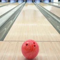 A bowling ball in a bowling center on synthetic flooring that looks like real wood using a standard house oil pattern.