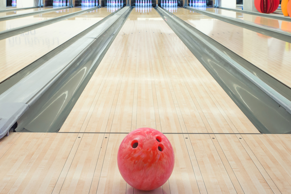 A bowling ball in a bowling center on synthetic flooring that looks like real wood using a standard house oil pattern.
