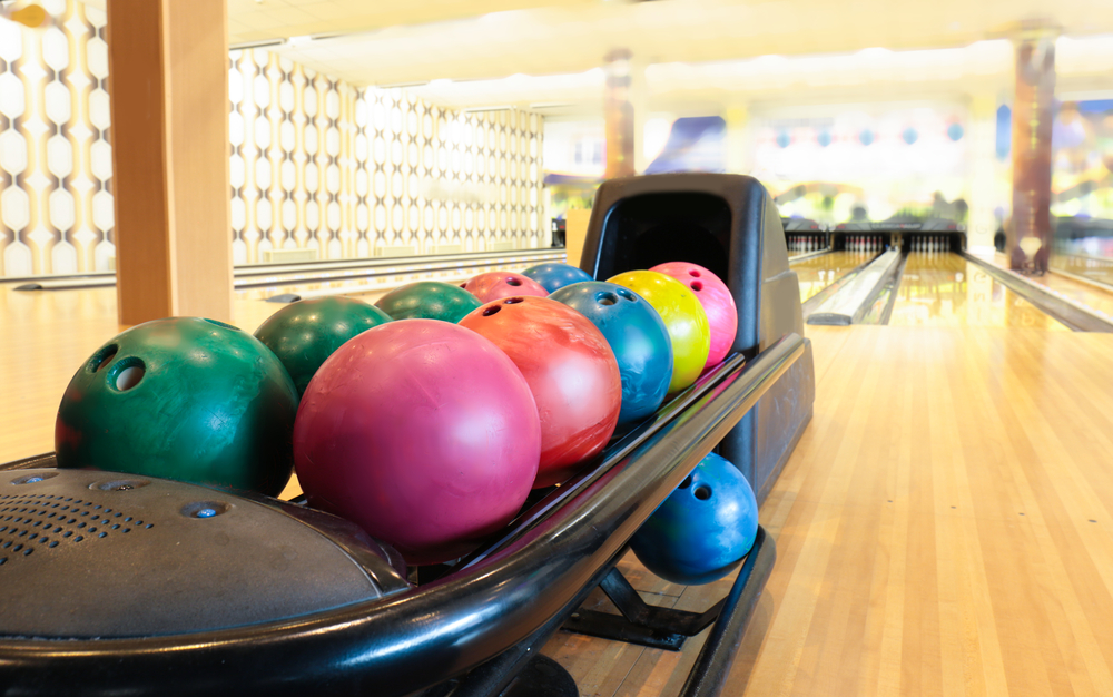 Several colorful bowling balls waiting in a ball return machine sitting on a freshly oiled wood floor.