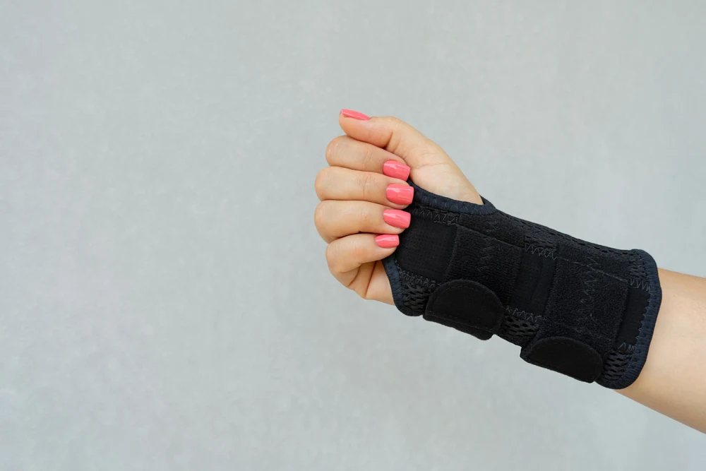 A woman with colored fingernails is wearing an orthopedic wrist brace to keep her wrist firm before going bowling.