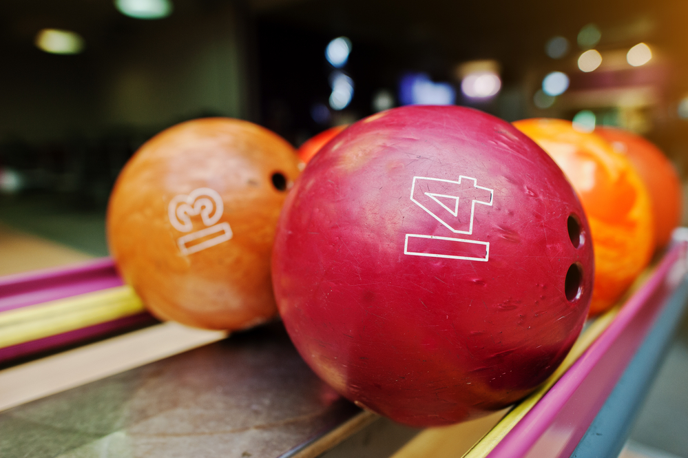 Red and orange bowling balls with numbers 14 and 13 sit in a local pro shop after being cleaned with a microfiber towel.