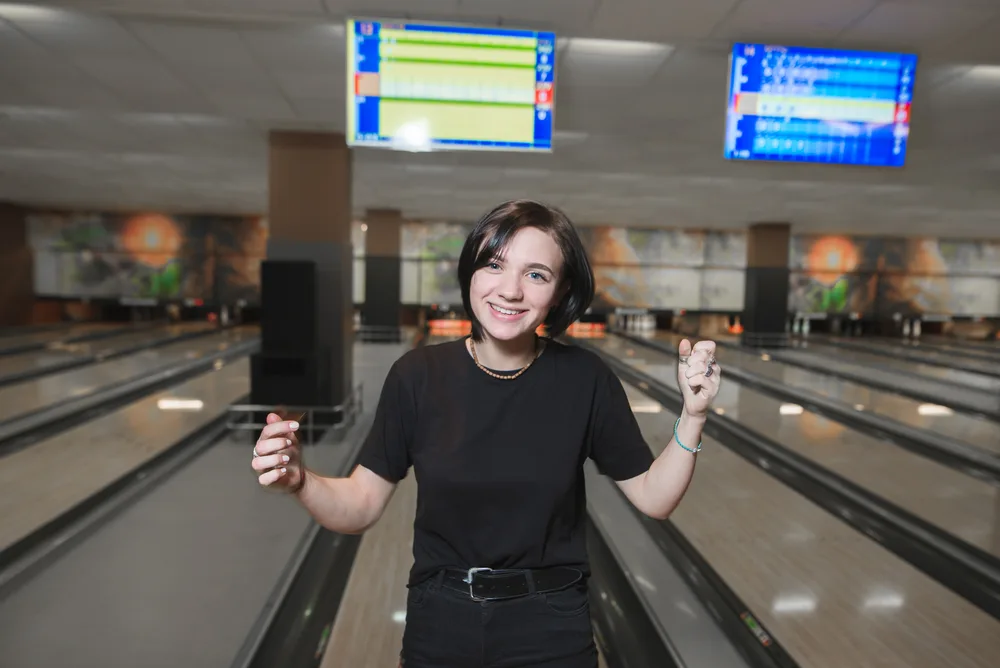 A lady wearing an all-black t-shirt and pants at the bowling alley is asking about maximum scores after missing a spare.