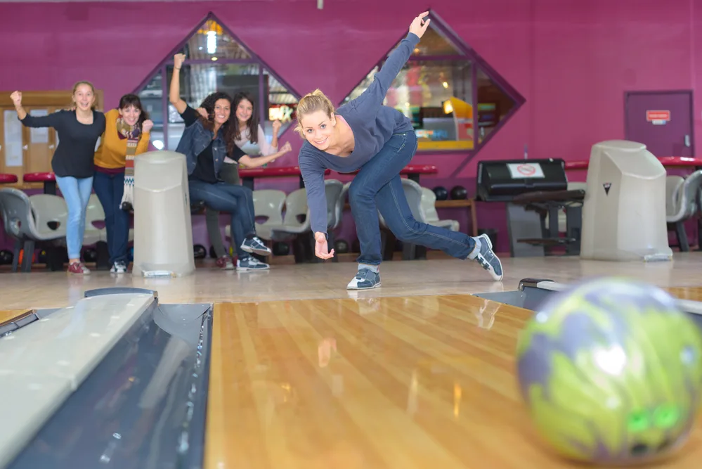The lady in the blue shirt rolled the ball using the bowling tips from her friends.