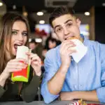 Girl and boy sitting at a table in the bowling alley eating as food or concessions is how bowling alleys make the majority of their money