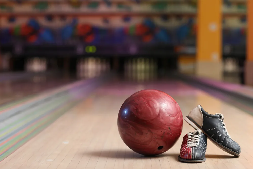 A read bowling ball and colorful shoes on a synthetic bowling lane at a local, family-friendly bowling alley.