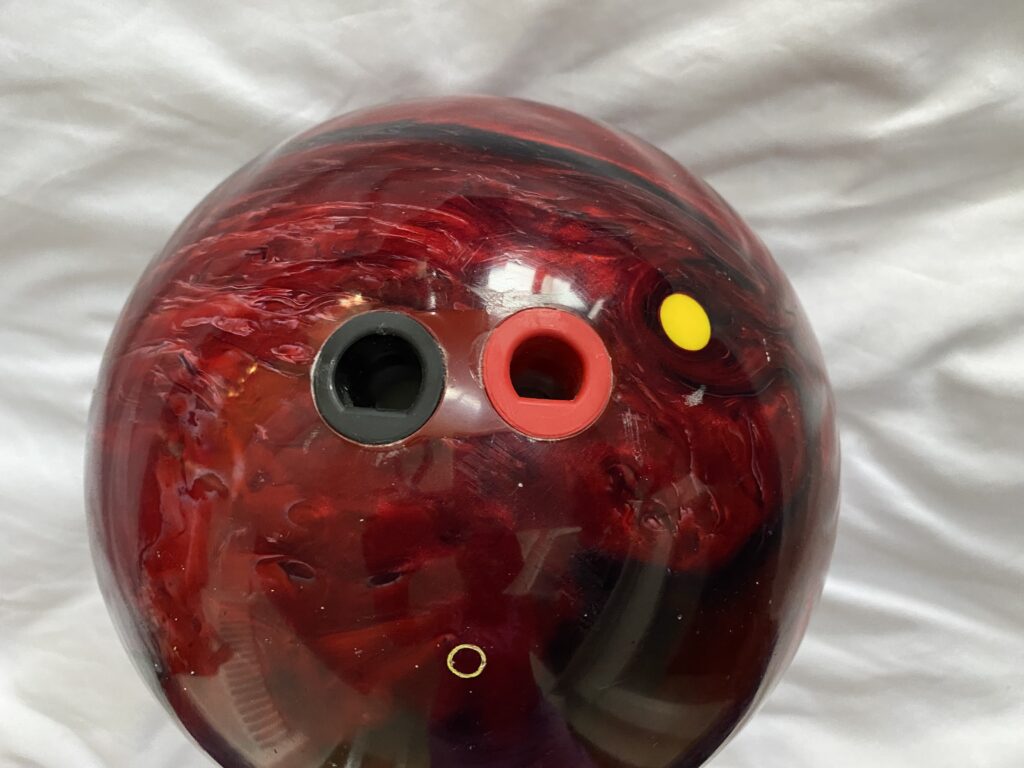 A black and red bowling ball with fingertip grip holes drilled that has thumb inserts giving pro bowlers more control.