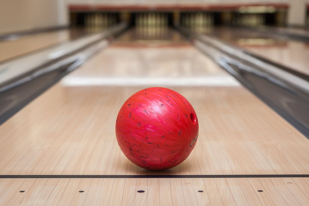 The red ball rolls down the lane with the finger holes and thumb holes visible following an open frame on a double wood lane.
