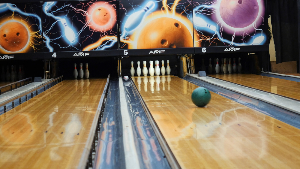 A colorful bowling ball rolls down a pine bowling lane where the entire lane is covered with a house oil pattern.