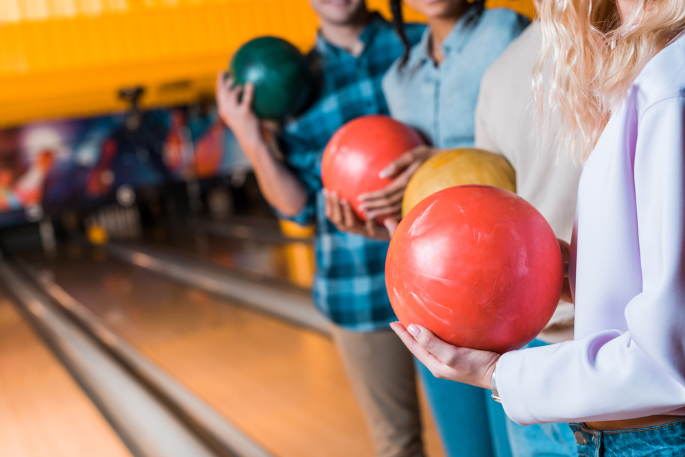 A group photo of several bowlers at the local bowling alley where a man in the back is holding a heavier bowling ball.