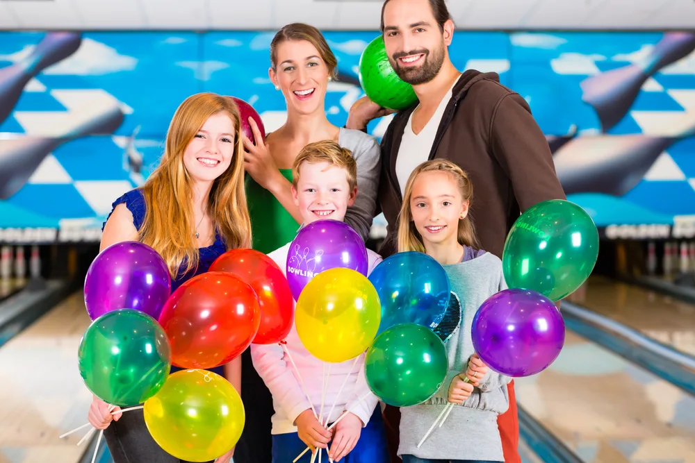 The parents holding the bowling balls enjoyed their spring fun pass friday play because it included bowling shoes.