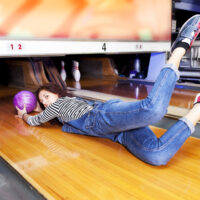 The bowler with a purple bowling ball crosses the foul line and heads toward the dangerous pin-setting machine.