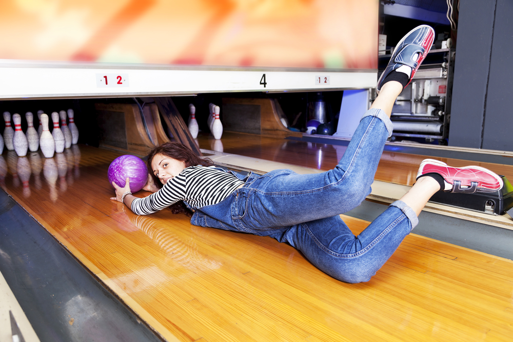 The bowler with a purple bowling ball crosses the foul line and heads toward the dangerous pin-setting machine.