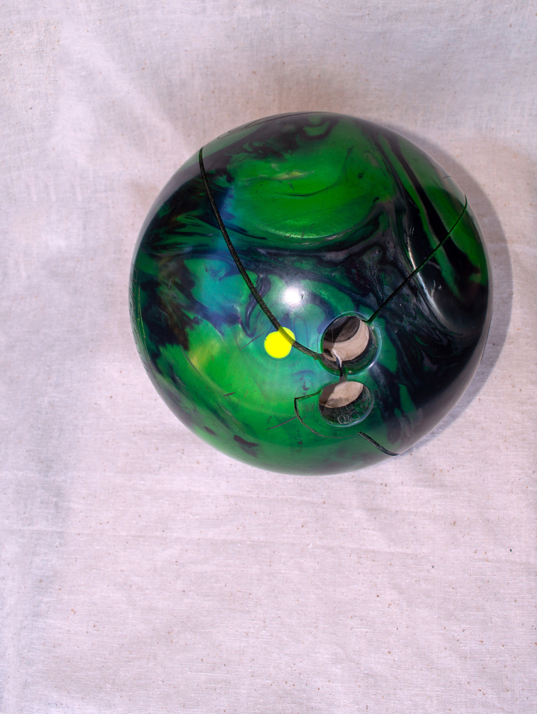 Green and blue bowling ball with cracks near finger holes- severely cracked bowling balls are in need of bowling ball repair kit