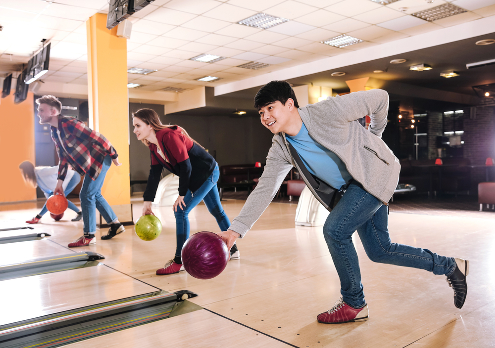 Four friends bowling shows good bowling etiquette and allows the bowler to the right to bowl first.
