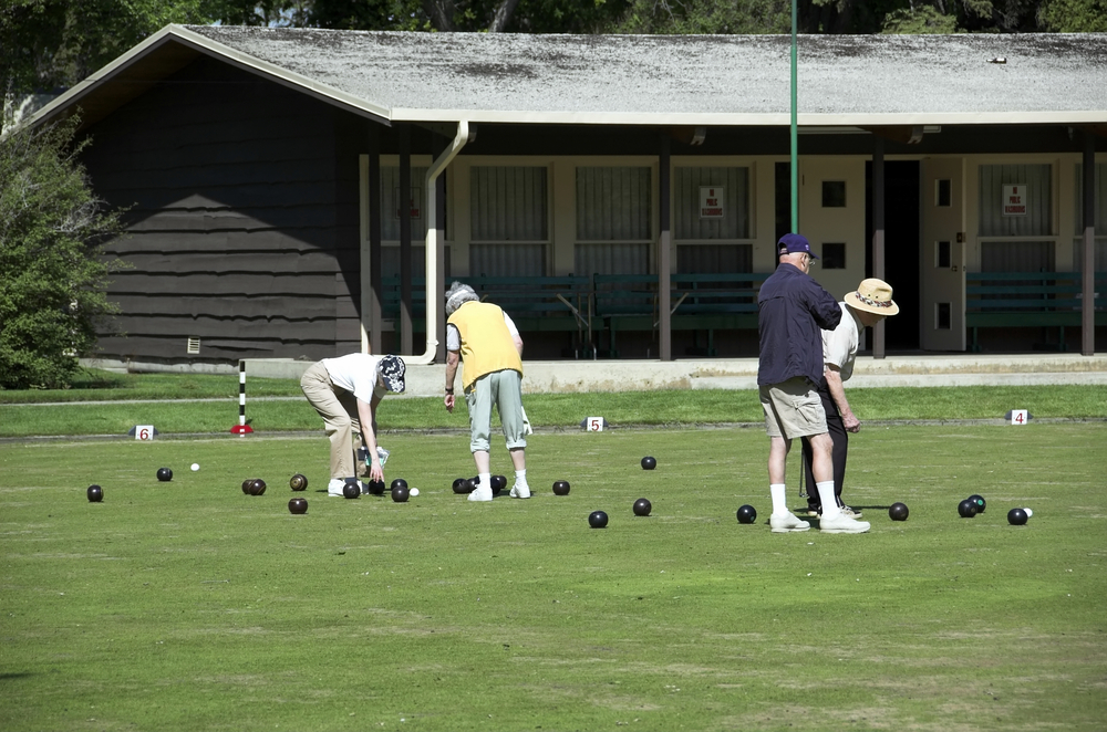 The men and women have grass as the playing surfaces in their game of bowls.