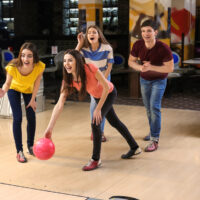 The bowler in the orange shirt is stepping with her left foot.