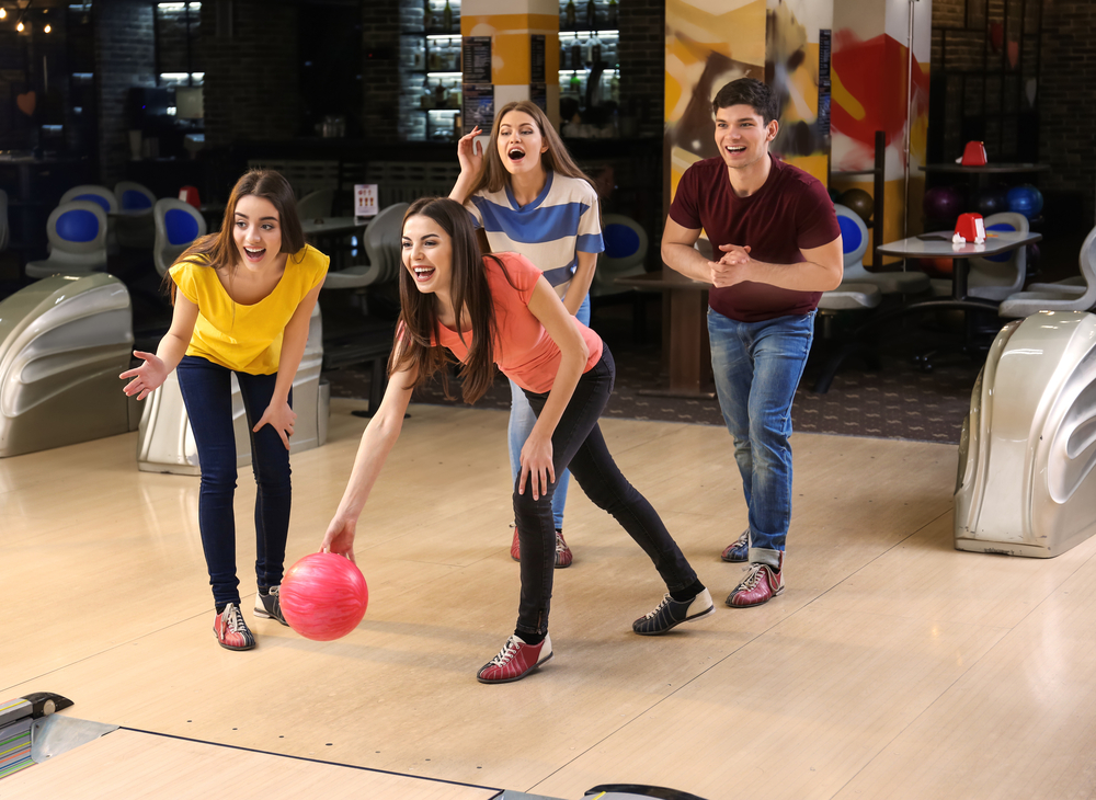 The bowler in the orange shirt is stepping with her left foot.
