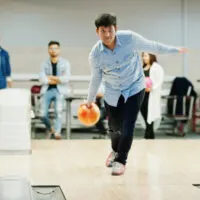 A south Asian man in jeans and button shirt is has his slide foot, slightly ahead of his right foot.