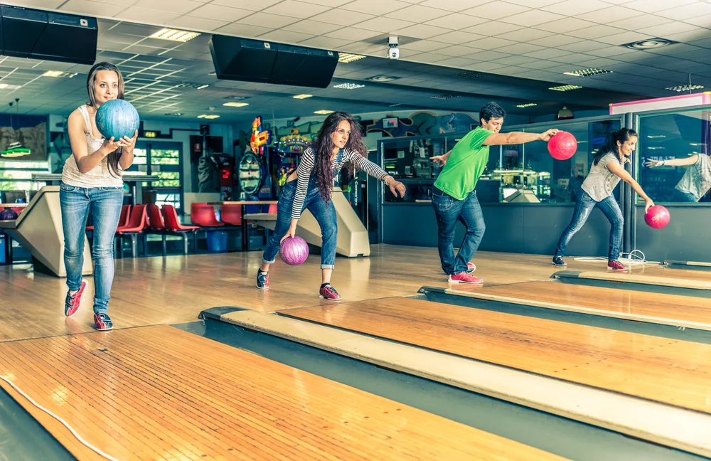 The woman bowler with the blue ball is conscience of her foot placement as she approaches the line.