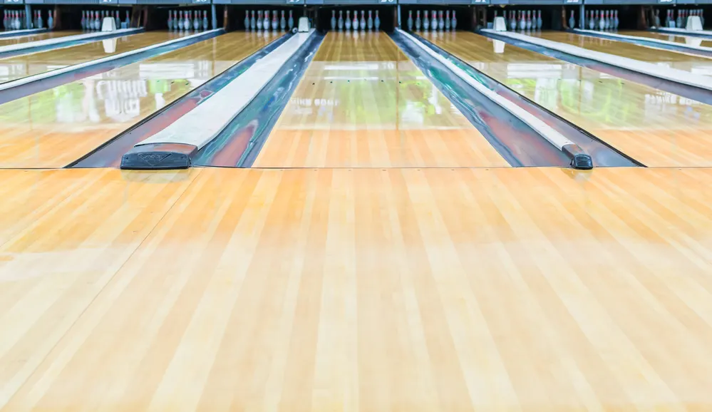 The oil on the floor slows down the acceleration of the bowling ball.