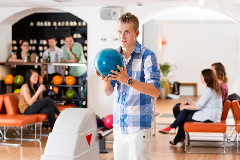 The bowler with the blue and white checkered shirt is practicing his stance to ensure he has good balance.