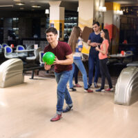 The bowler in the burgundy shirt has the ball in their right hand and stepped with their left leg.