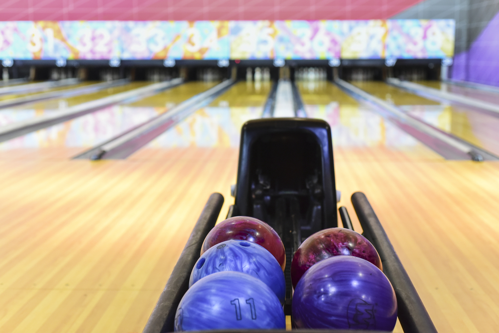 Each lane has a different number of bowling pins remaining, with various colored bowing balls on the ball return.